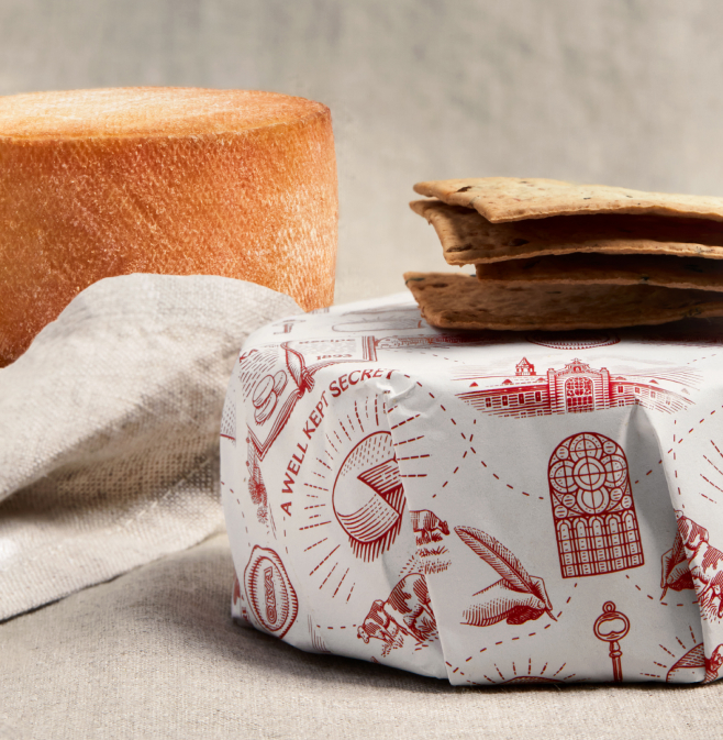 Two Cheese wheels, one in the foreground, wrapped, with crackers stacked on top